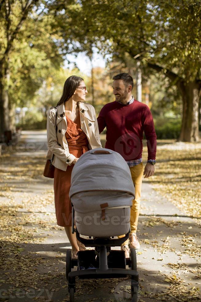 glada unga föräldrar som går i parken och kör en baby i barnvagn foto