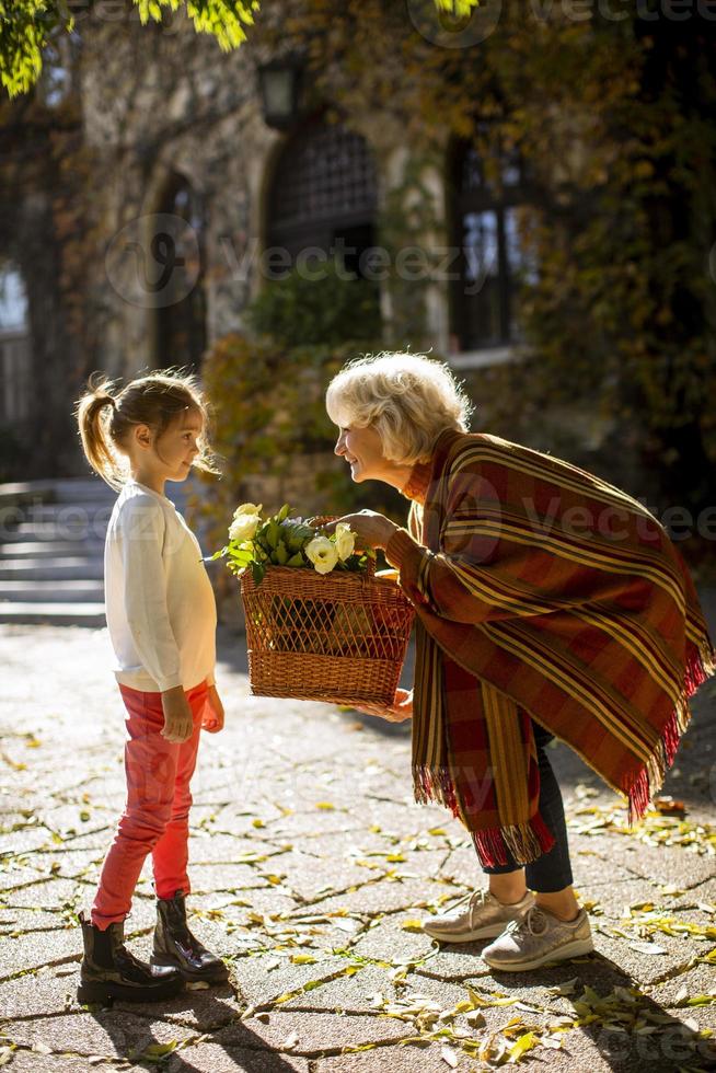 mormor har roligt med sitt lilla barnbarn och håller korgen full med blommor foto