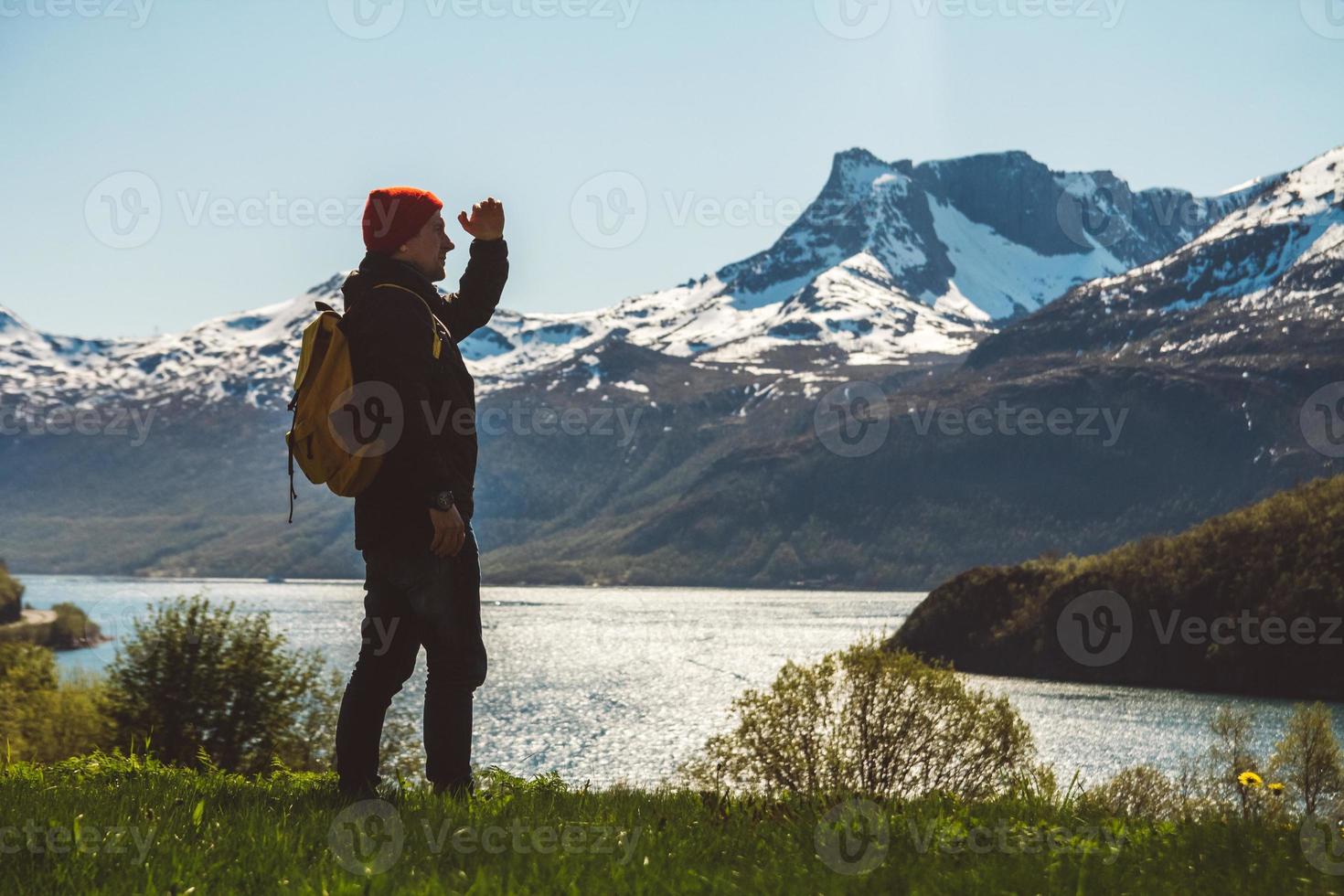 ung man med en ryggsäck som står på bakgrunden av berg och sjö. utrymme för ditt textmeddelande eller reklaminnehåll. resa livsstilskoncept foto