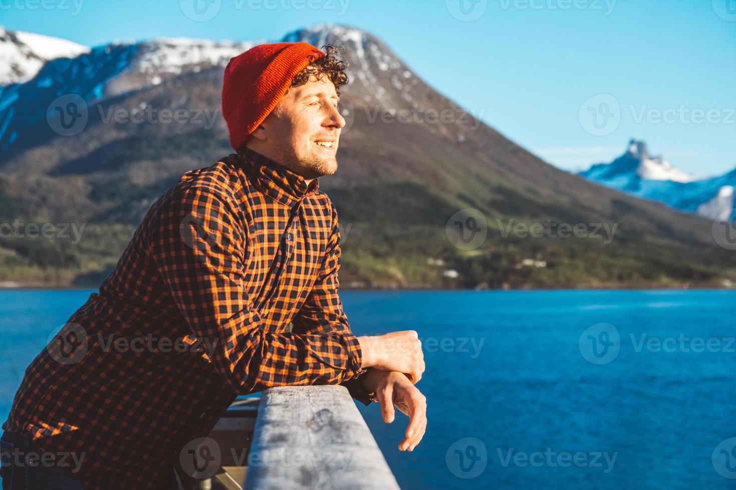 porträtt av ung man som står på en träbrygga på bakgrund av berg och sjö. plats för text eller reklam foto