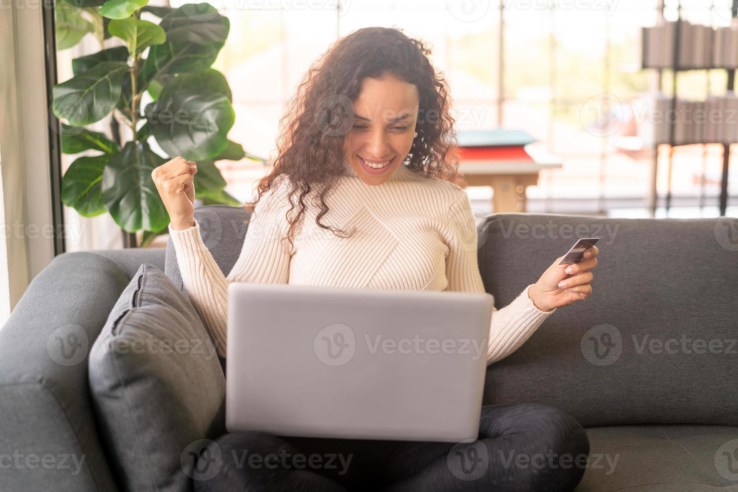 latinsk kvinna som använder bärbar dator och hand som håller kreditkort för att shoppa på soffan foto