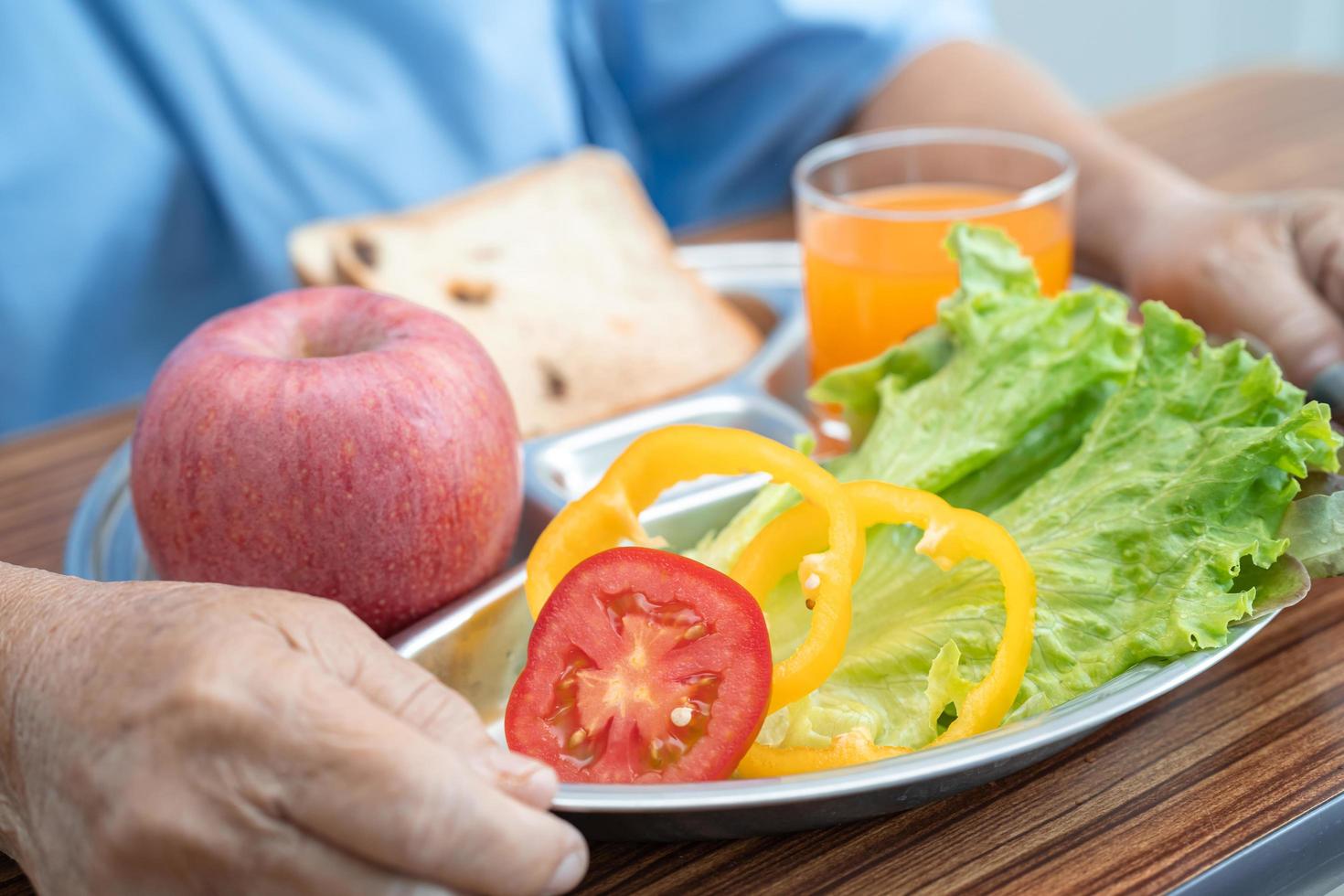 asiatisk senior eller äldre gammal damkvinna som äter frukost vegetabilisk hälsosam mat med hopp och lycklig medan du sitter och är hungrig på sängen på sjukhus. foto