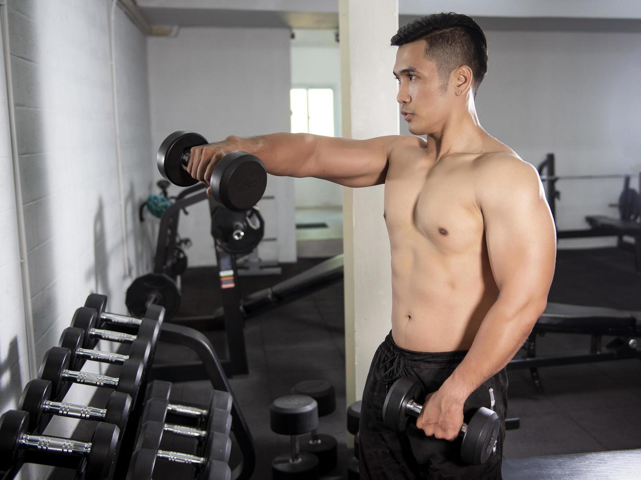 muskulös fitness man bodybuilder är träning med hantlar i gymmet foto