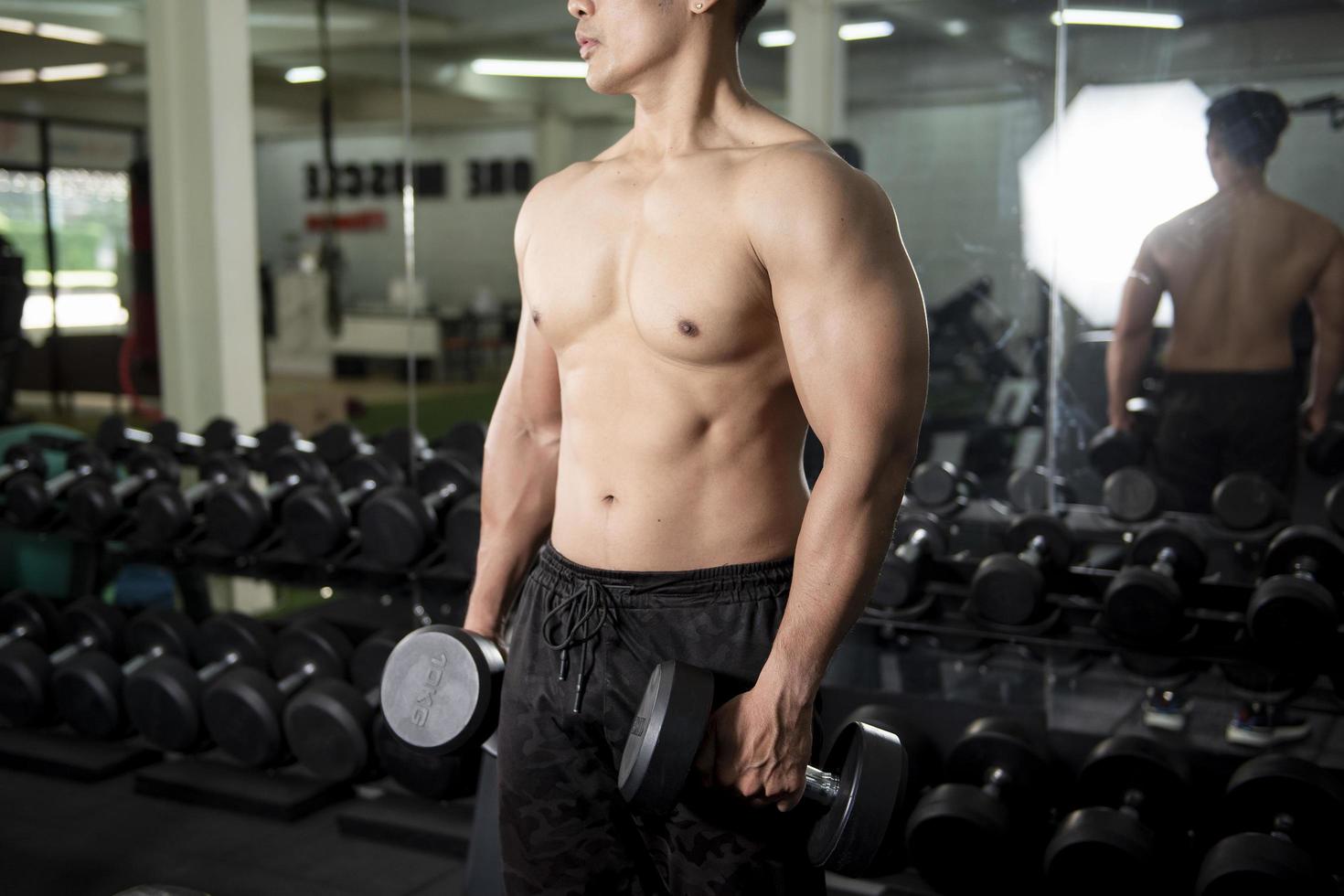 muskulös fitness man bodybuilder är träning med hantlar i gymmet foto