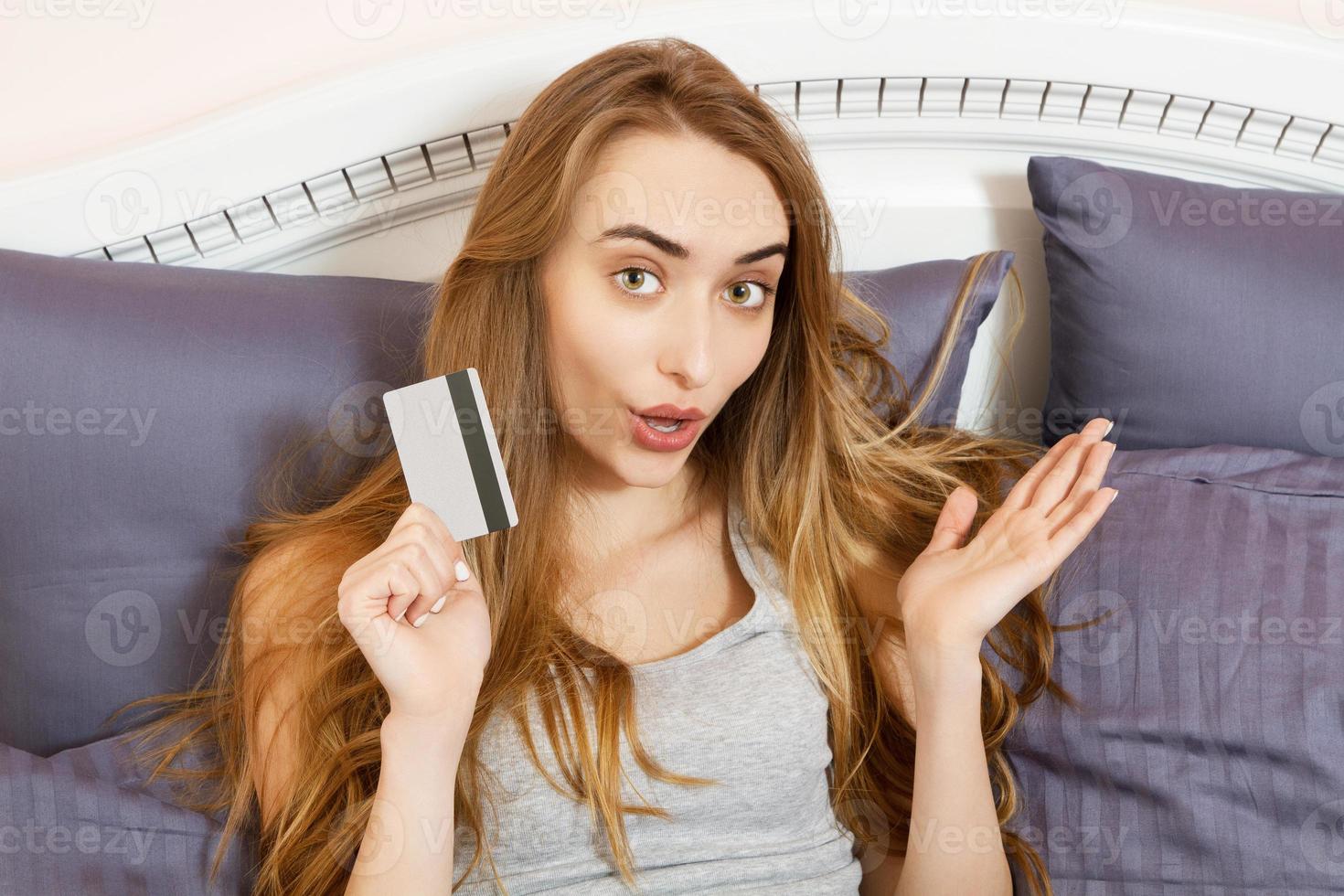 leende känslomässig kvinna shopping på internet håller bankkort och hon liggande på sängen hemma. asiatisk tjej köper online med kreditkort hon är i sängen. foto
