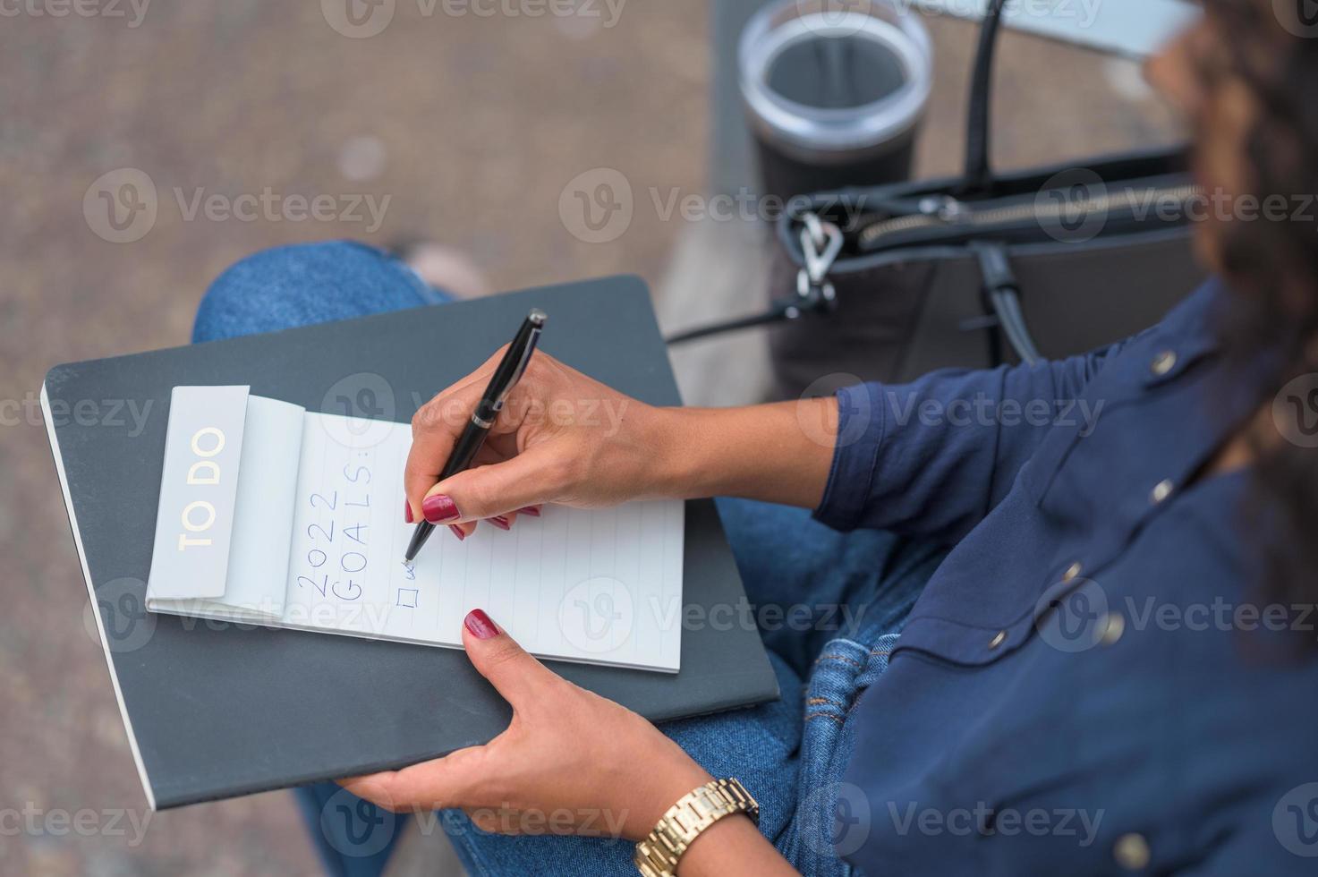 svart kvinna med rött nagellack skriver sitt nyårslöfte i en att göra-lista med en svart penna foto