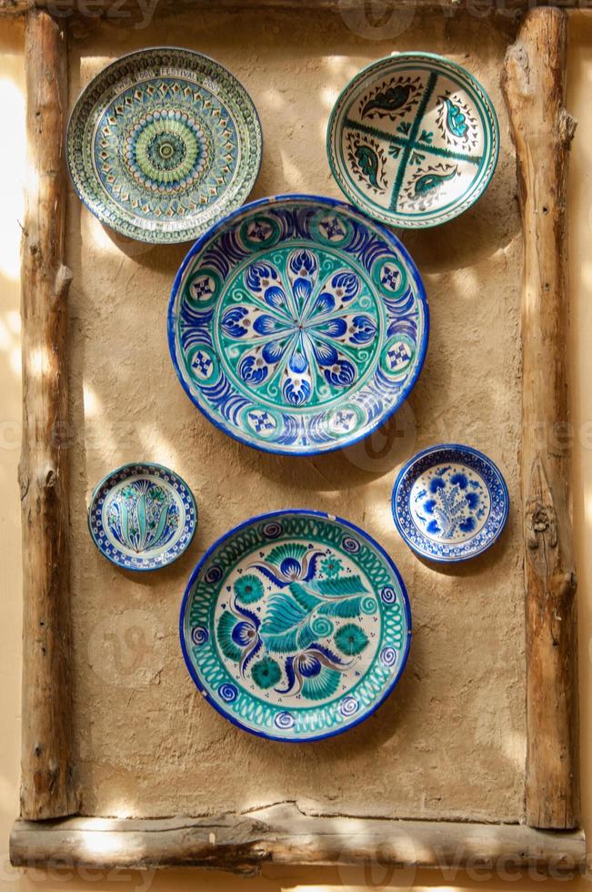 östra keramiska plattor hänger på en lervägg. väggen av lera är dekorerad i orientalisk stil med en keramisk platta och träklossar foto