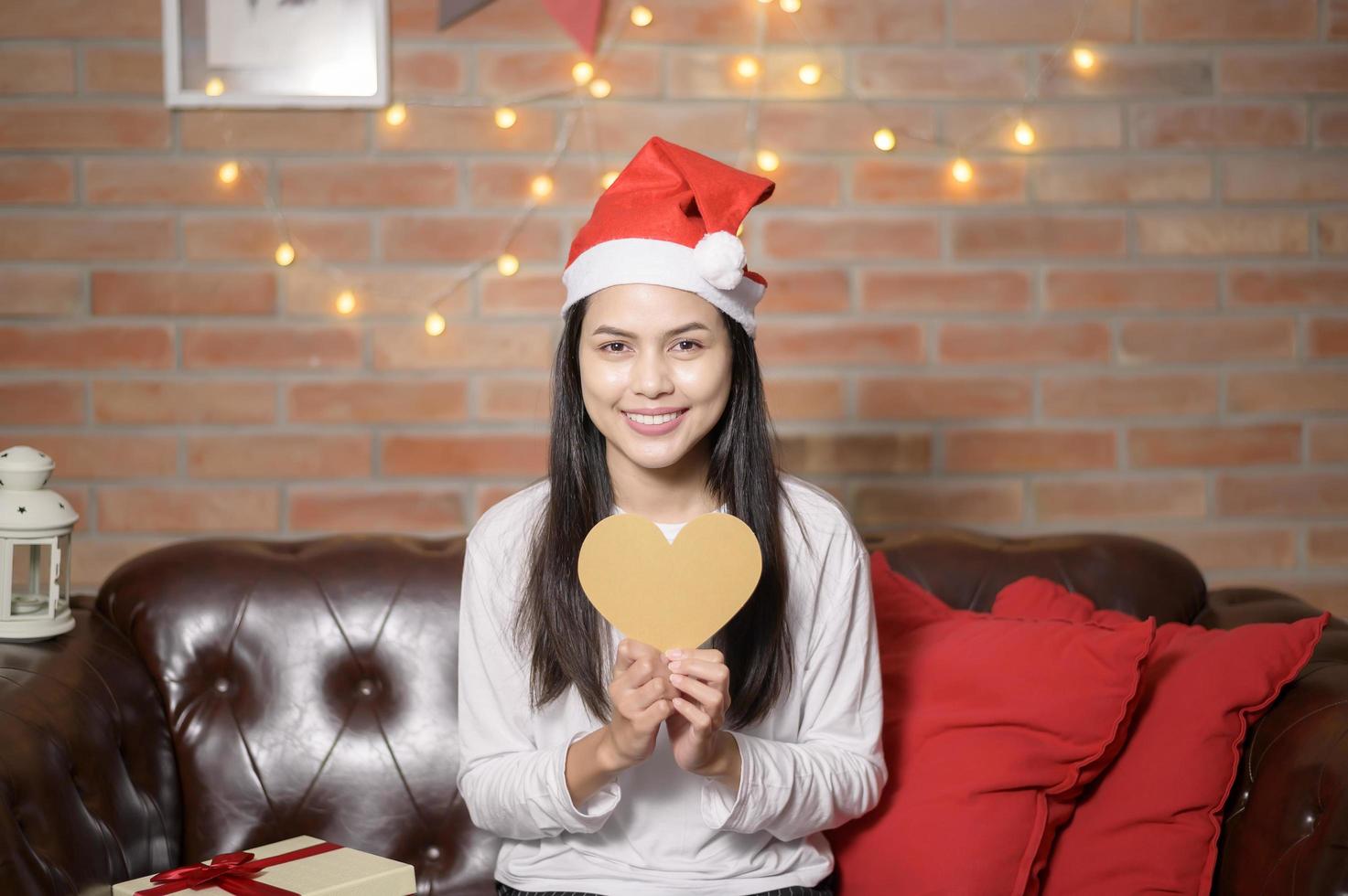 ung leende kvinna som bär röd jultomtehatt som visar en hjärtformad modell på juldagen, semesterkoncept. foto