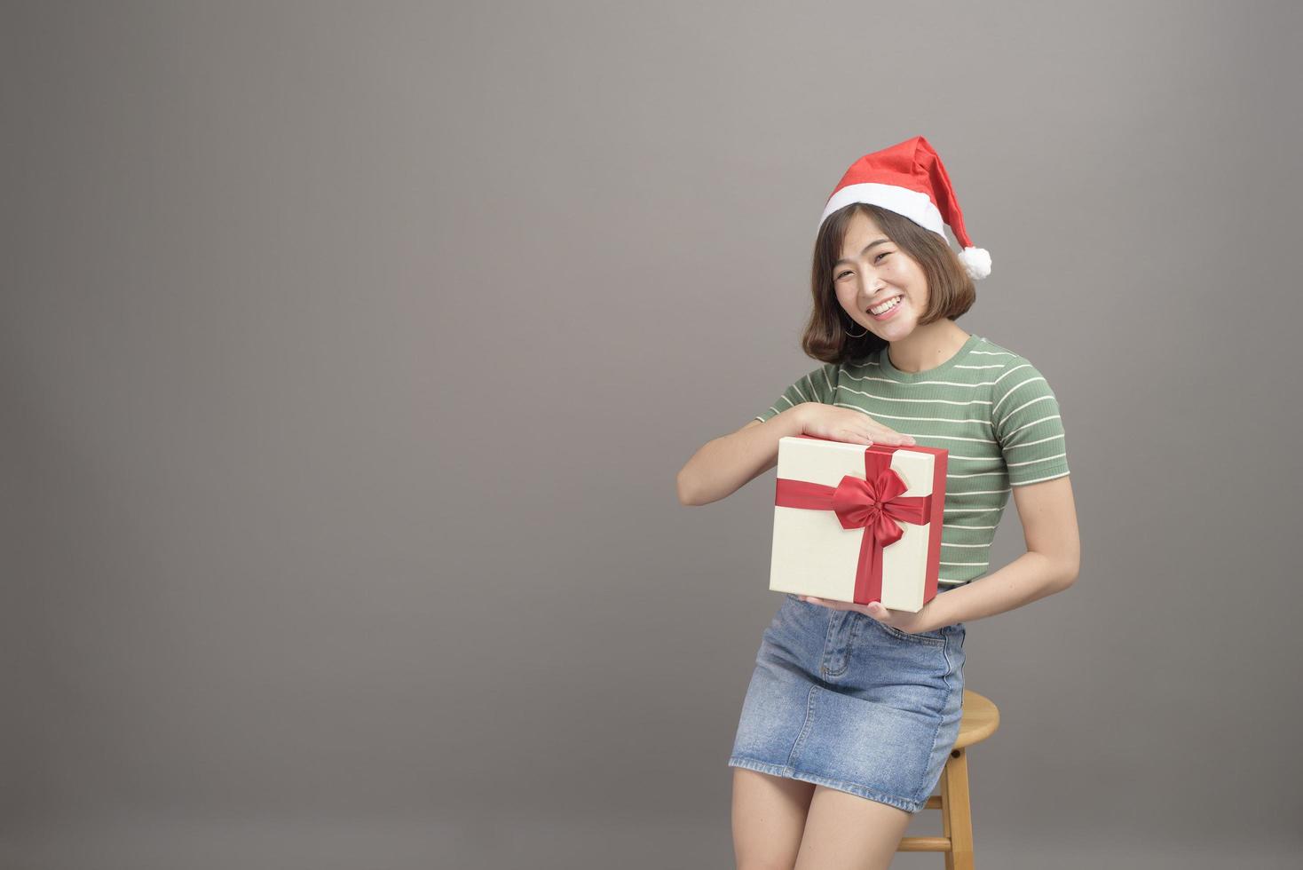 porträtt av vacker kvinna som bär röd jultomtehatt som håller presentask över studiobakgrund, jul- och nyårskoncept foto