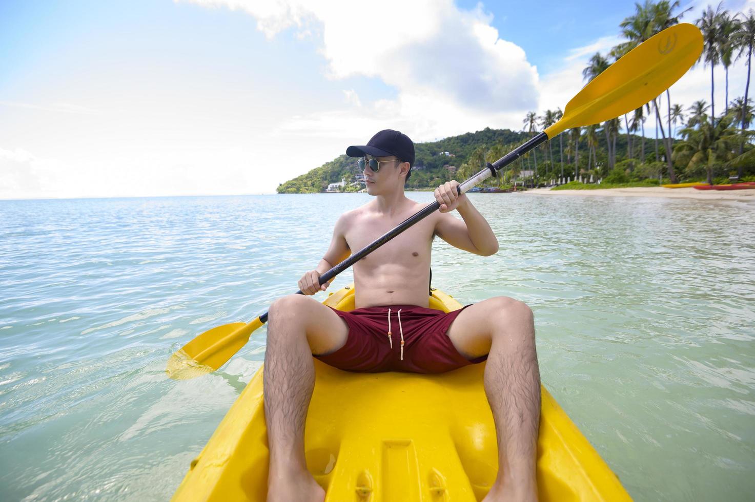 en ung sportig man som paddlar kajak vid havet i en solig dag foto