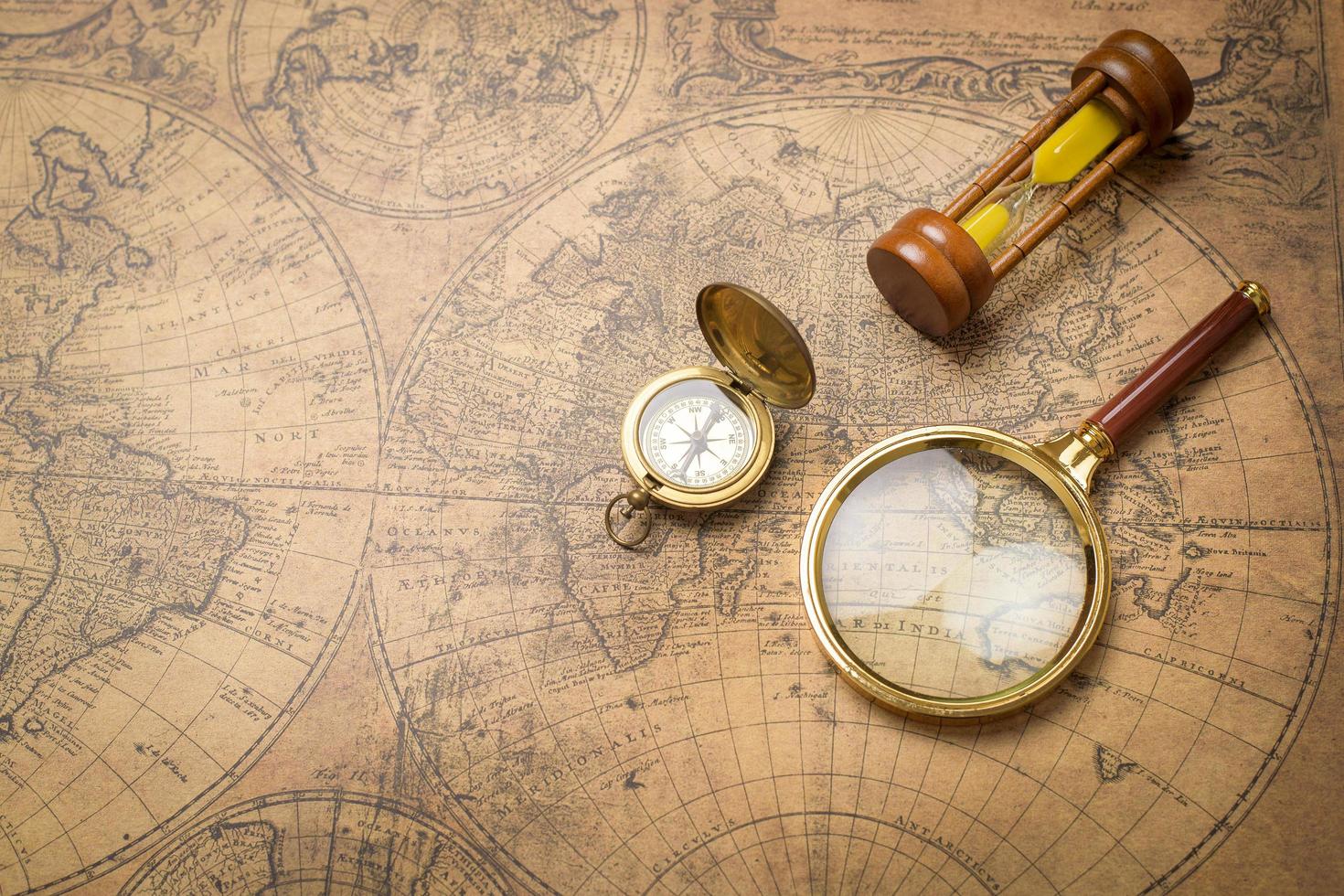 gammal kompass, förstoringsglas och sandklocka på vintagekarta foto