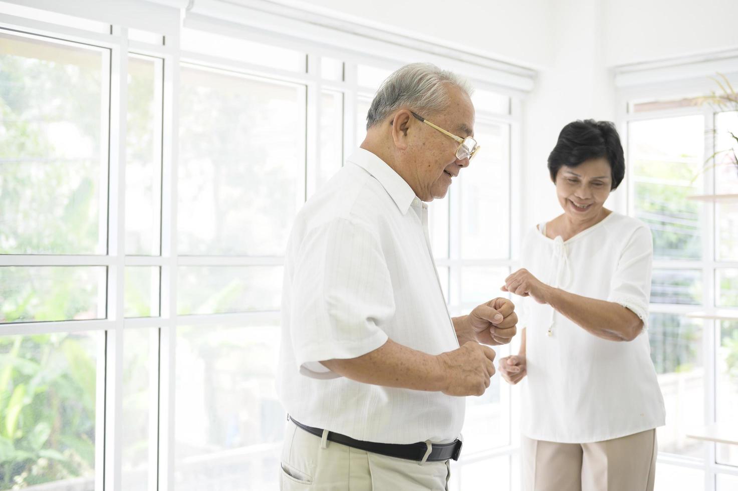 glada seniora asiatiska pensionerade par dansar och njuter av musiken i vardagsrummet hemma, hälsokoncept foto