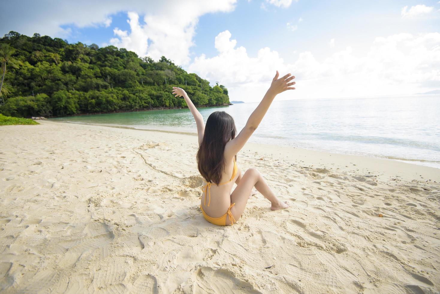 en glad vacker kvinna i gul bikini njuter och kopplar av på stranden, sommaren och semesterkonceptet foto