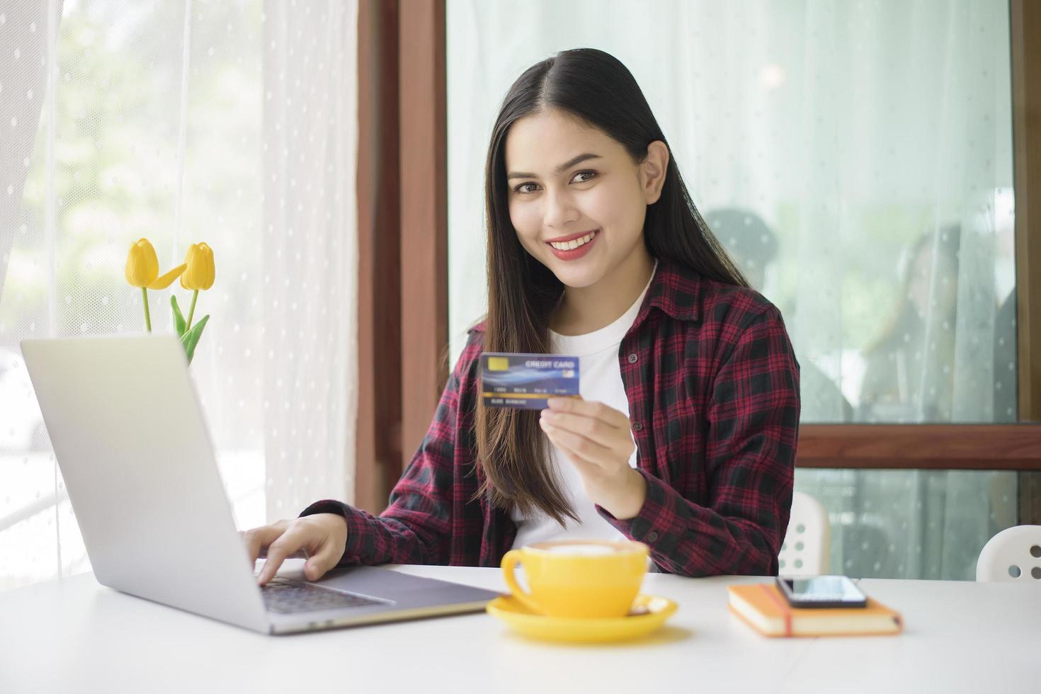vacker kvinna är onlineshopping med kreditkort i kaféet foto