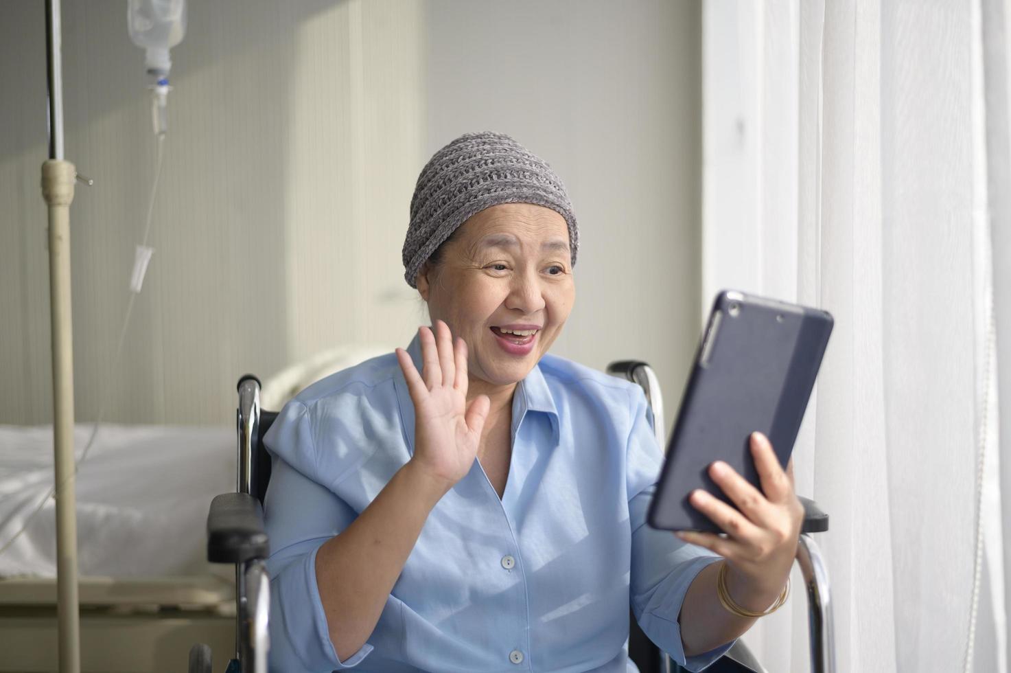 cancerpatient kvinna som bär huvudduk ringer videosamtal på sociala nätverk med familj och vänner på sjukhus. foto