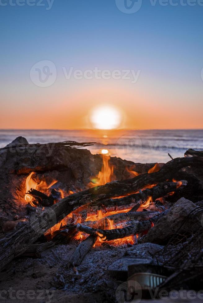 brasa med brinnande ved under vacker solnedgång på stranden foto