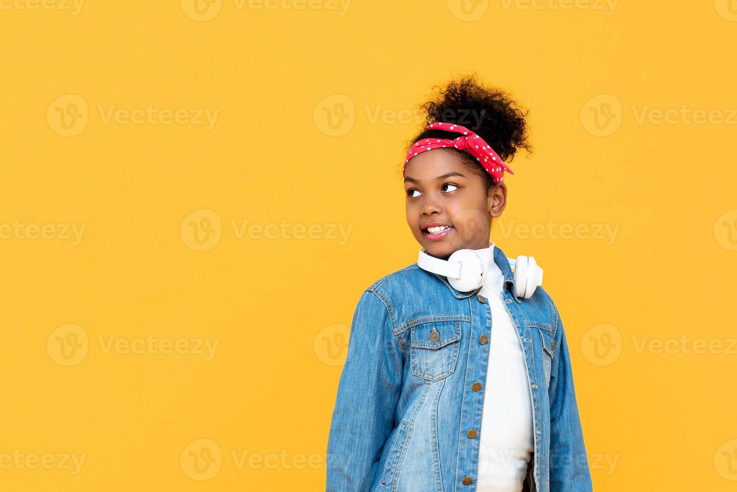 leende moderiktig blandad afrikansk flicka tittar på kopia utrymme åt sidan studiobild isolerad på färgglad gul bakgrund foto