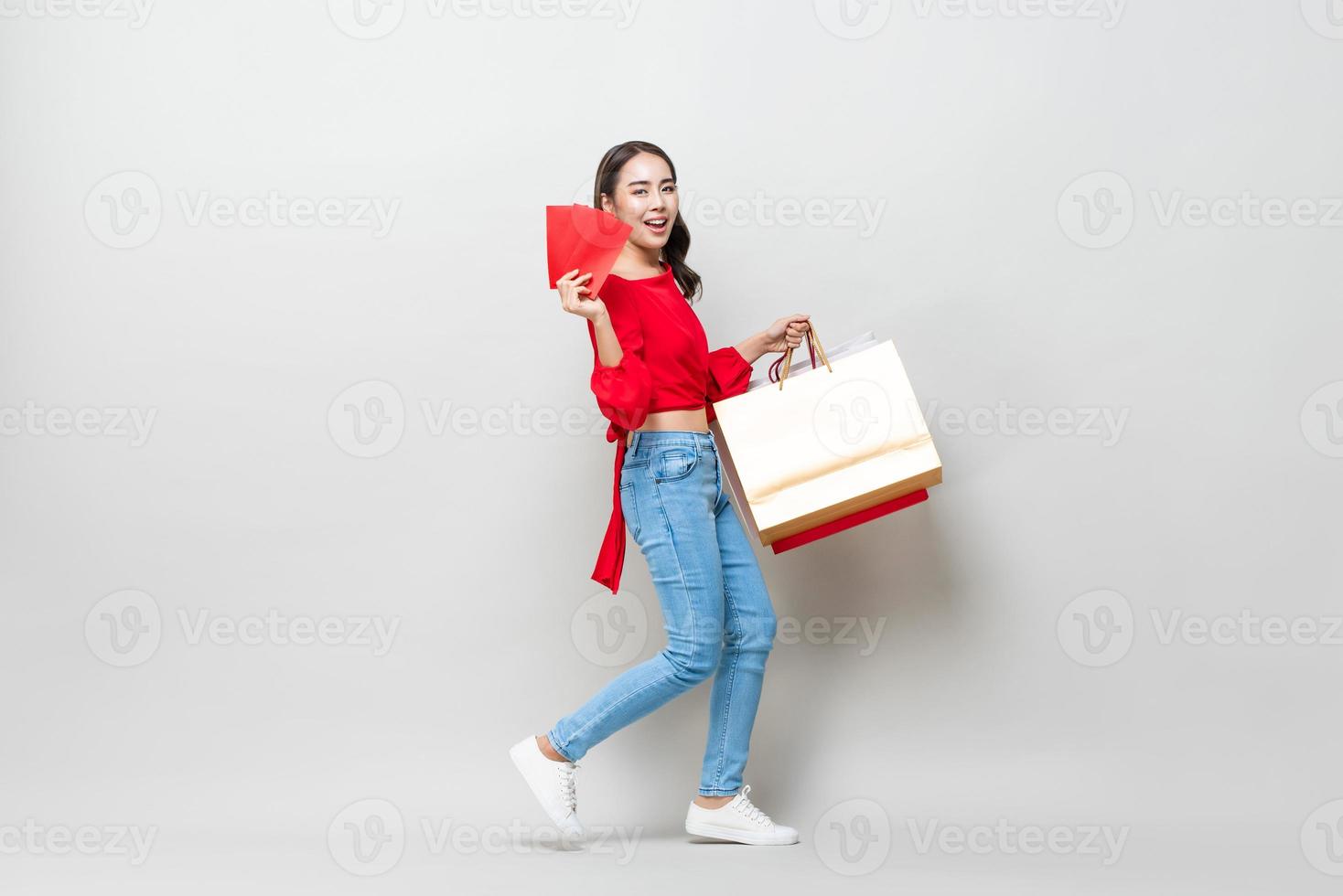 glad asiatisk kvinna som håller shoppingkassar och röda kuvert eller ang pao isolerad i ljusgrå studiobakgrund för försäljningskoncept för kinesiskt nyår foto