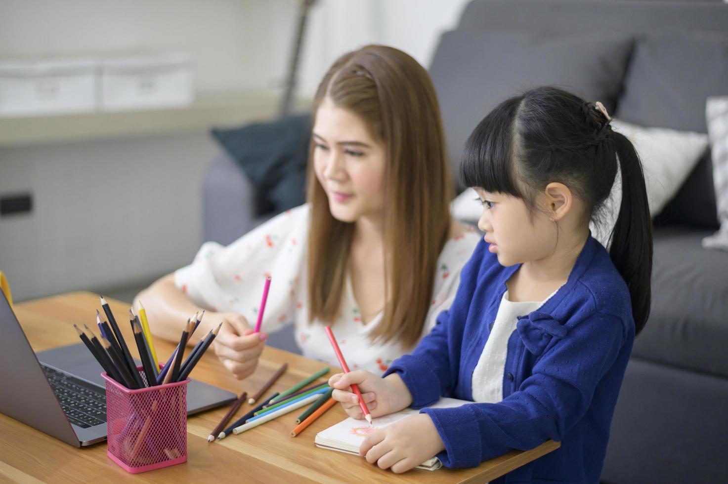 asiatisk glad mamma och dotter använder laptop för att studera online via internet hemma. e-lärande koncept under karantän. foto