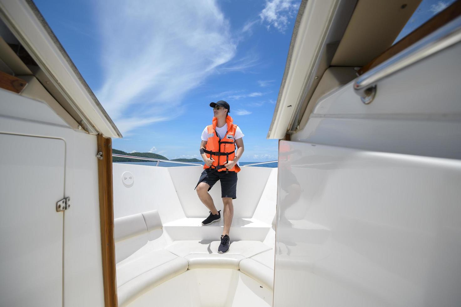 turist i flytväst njuter och kopplar av på motorbåt med en vacker utsikt över havet och bergen i bakgrunden foto