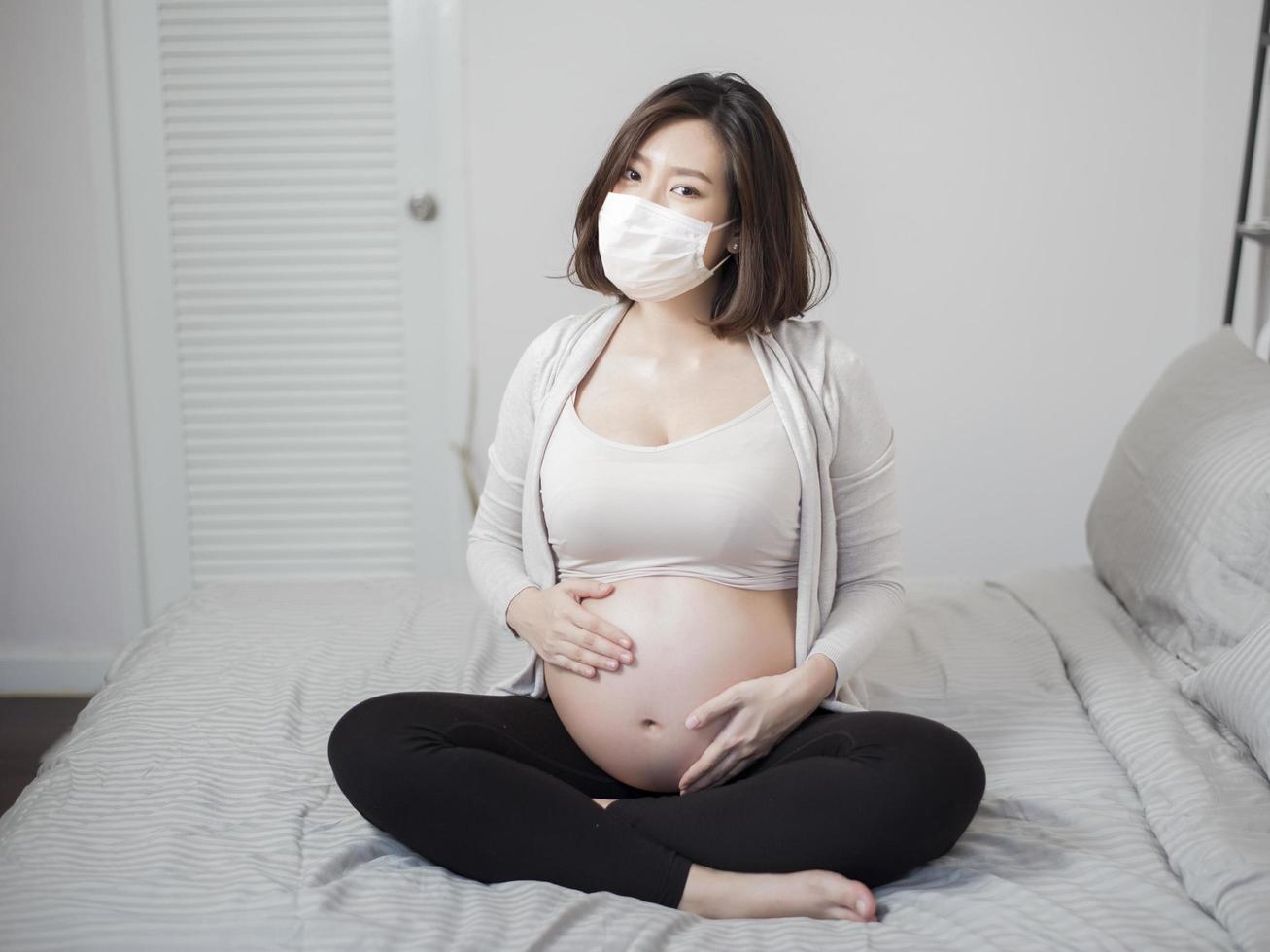 vacker asiatisk gravid kvinna bär skyddsmask i sitt hem, coronavirusskyddskoncept foto