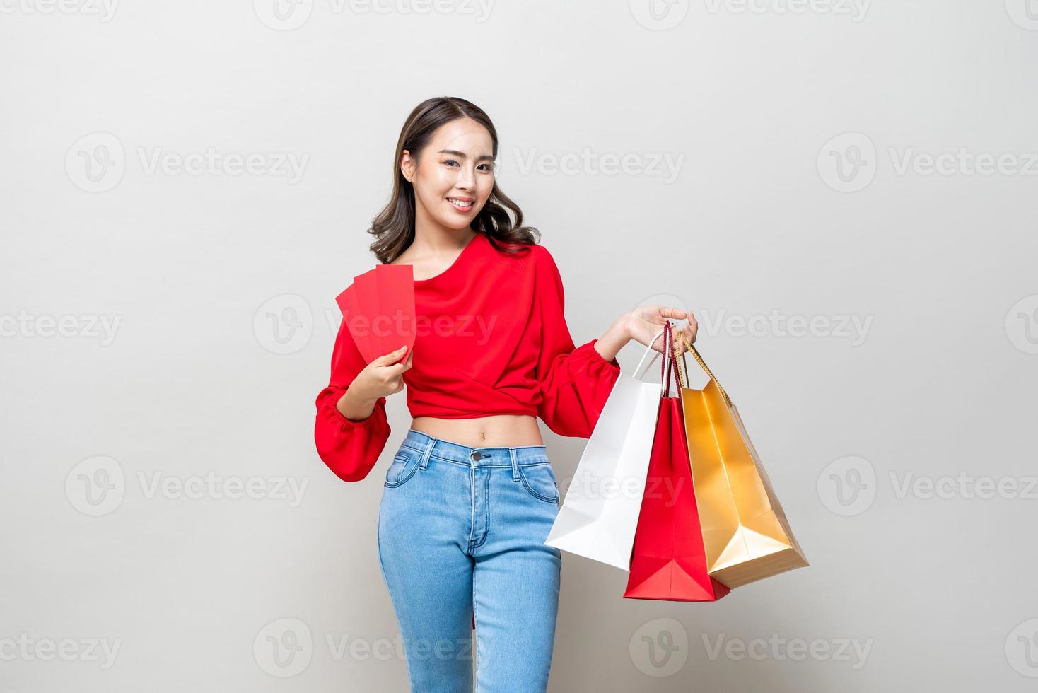 glad asiatisk kvinna som håller shoppingkassar och röda kuvert eller ang pao isolerad i ljusgrå studiobakgrund för försäljningskoncept för kinesiskt nyår foto