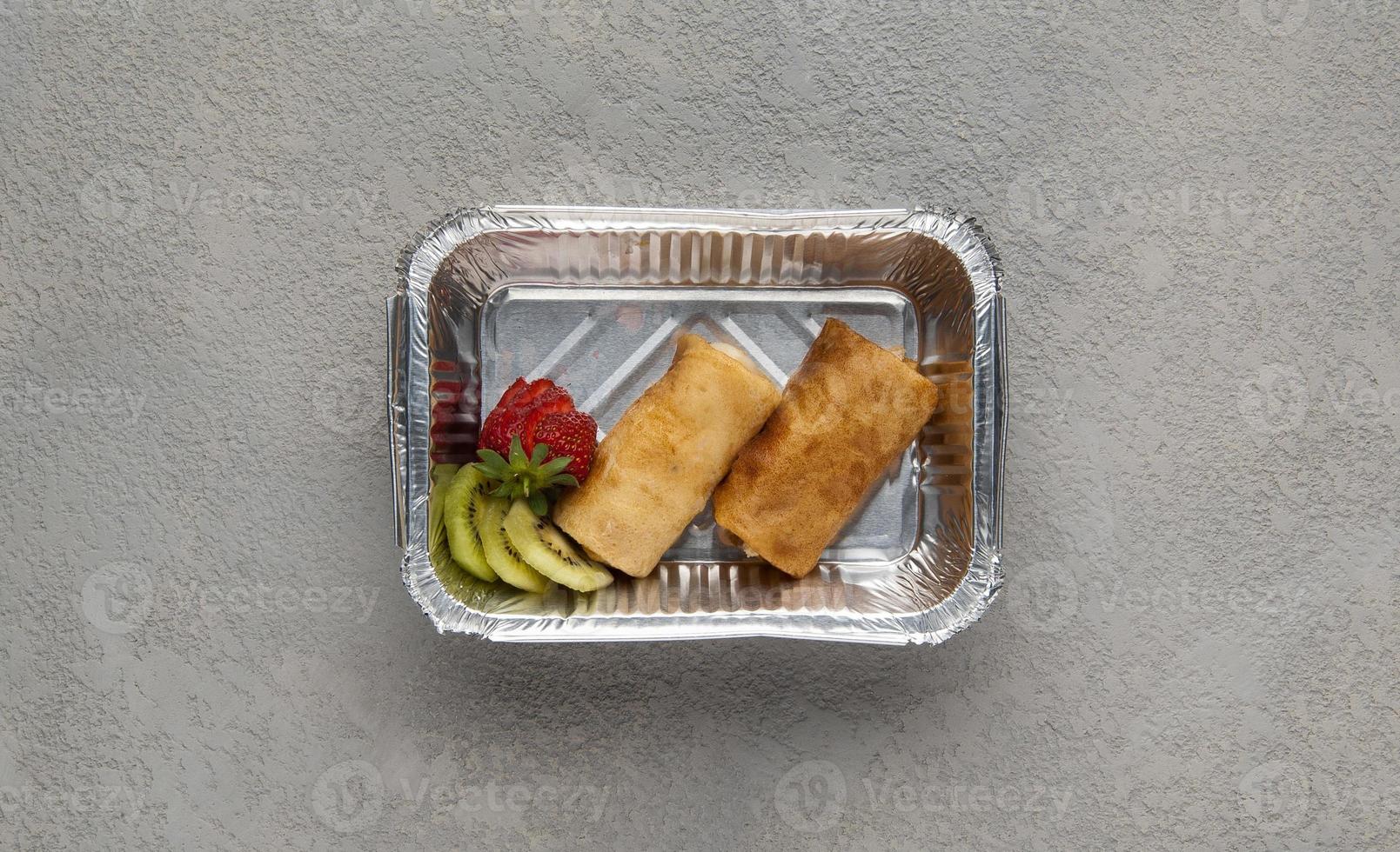snabbmat i en folielåda på en grå bakgrund. en hälsosam mat på nära håll foto