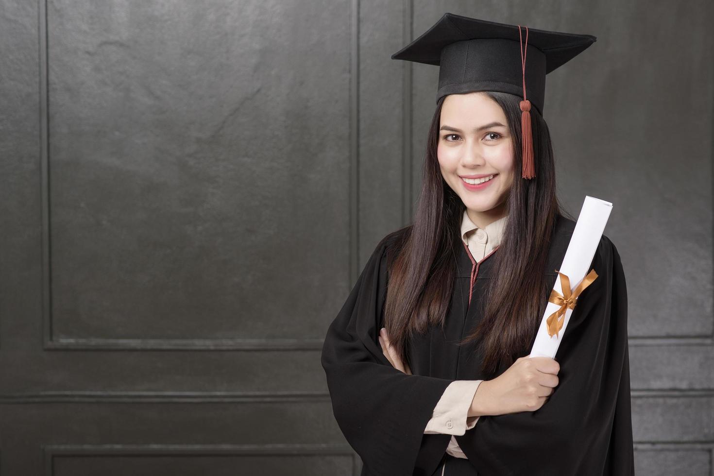 porträtt av ung kvinna i examen klänning ler och hejar på svart bakgrund foto