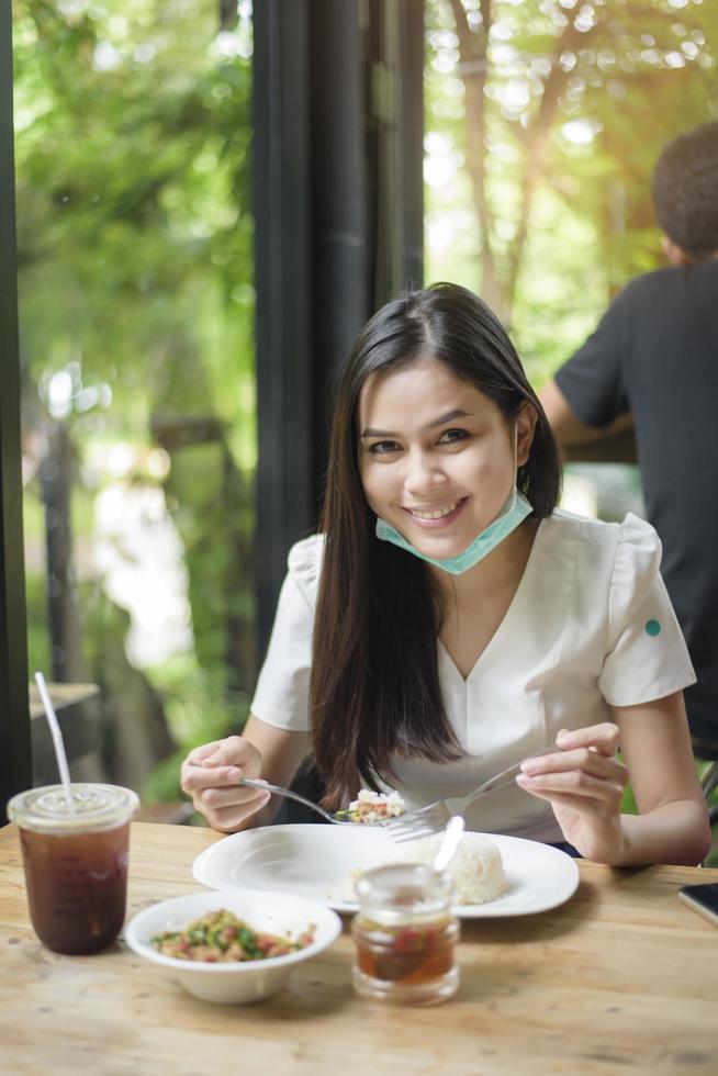 ung kvinna med ansiktsmask äter mat i restaurangen, nytt normalt koncept. foto