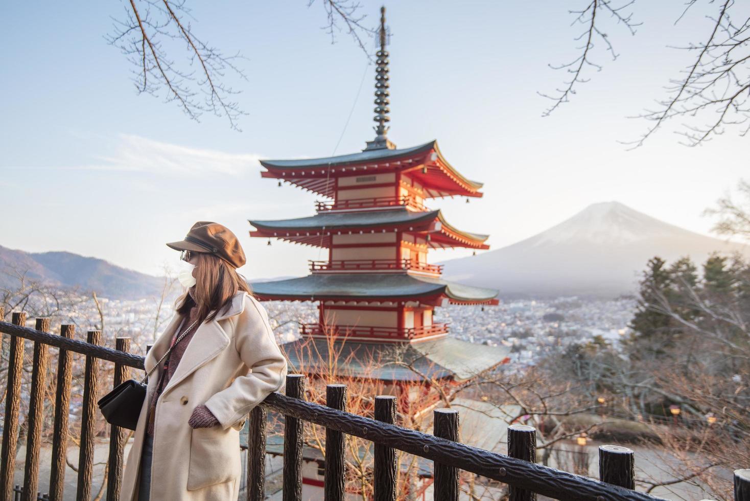vacker kvinna turist bär ansiktsmask på chureito-pagoden och fujiberget, Japan, resa under covid-19 pandemikoncept foto