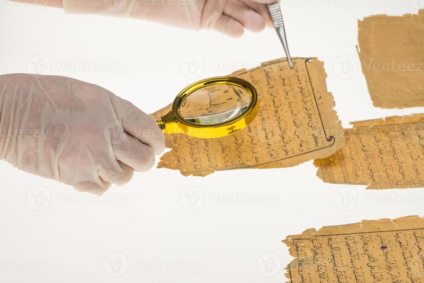 en forskare studerar arabisk skrift från Koranen med hjälp av ett förstoringsglas och ett bord med ljus. paleografi, studiet av forntida arabisk skrift foto