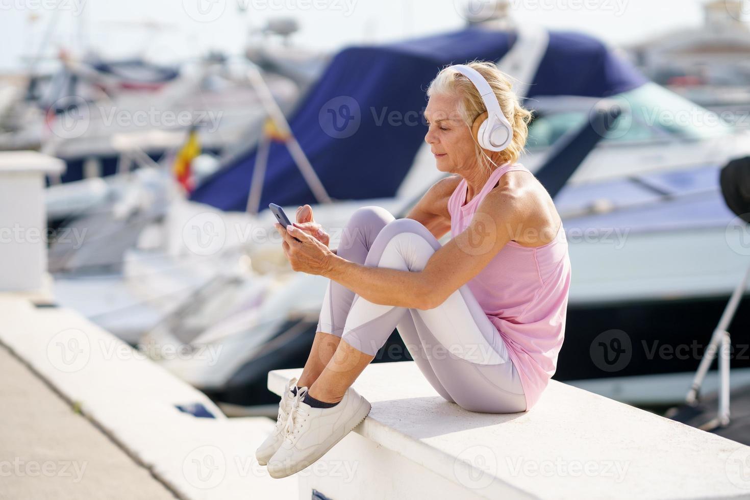 mogen sportig kvinna tar en paus för att kolla en träningsapp på sin smartphone foto