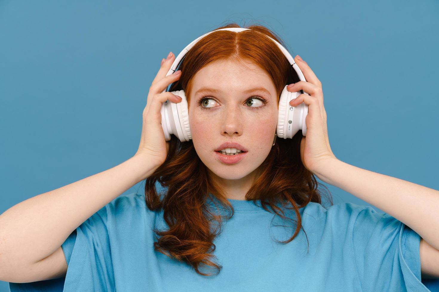 ung ingefära kvinna i t-shirt lyssnar musik med hörlurar foto