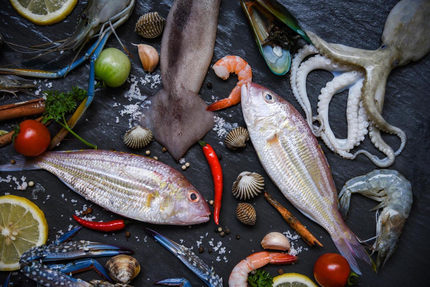 färska råa skaldjur med örter och kryddor citron på mörk bakgrund skaldjurstallrik med skaldjur räkor räkor krabbaskal foto