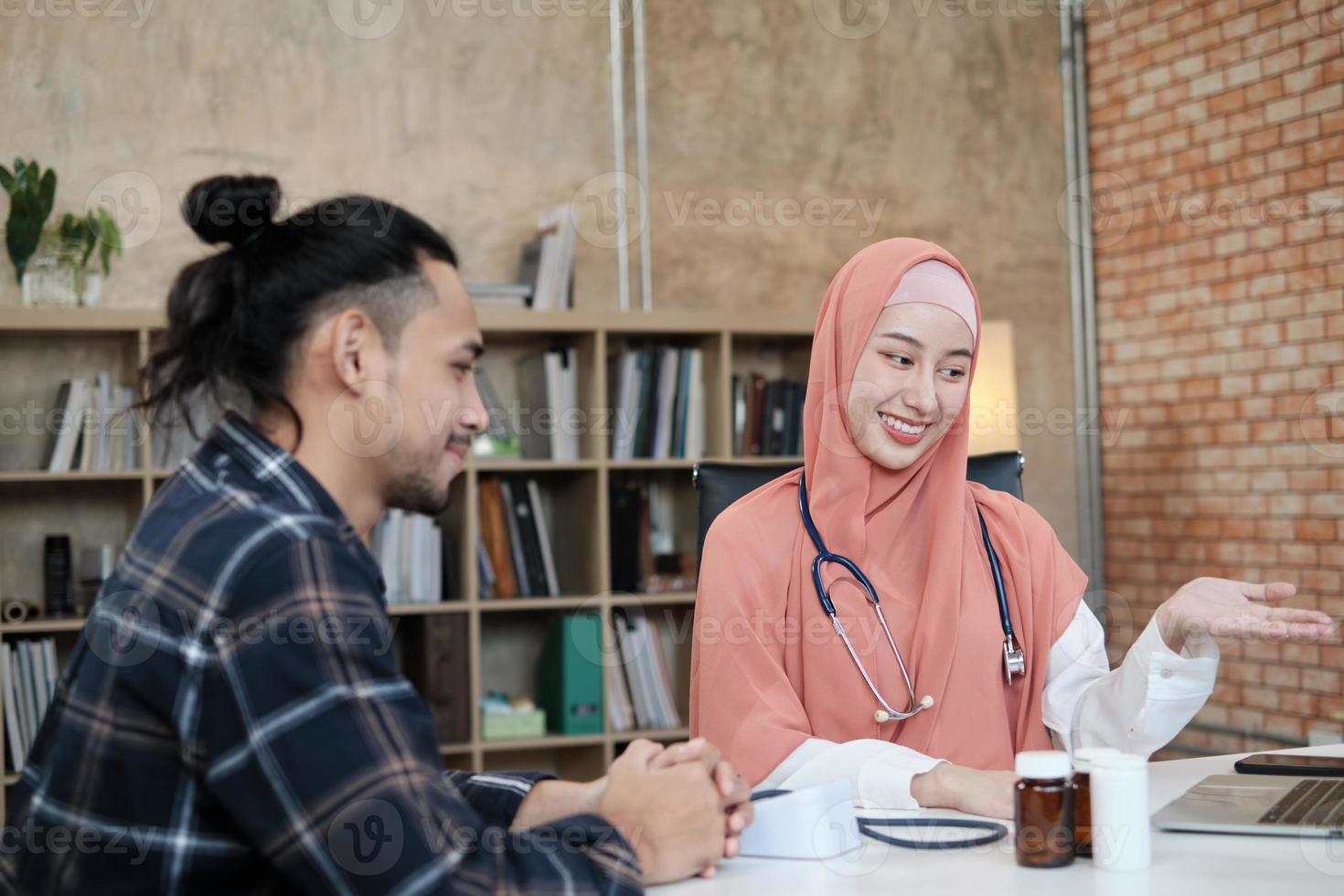 ung vacker kvinnlig läkare är hälsoundersökning manlig patient på kontoret på sjukhuskliniken och rådgör med ett leende om läkemedel. denna asiatiska medicinska specialist är en islamisk person som bär hijab. foto