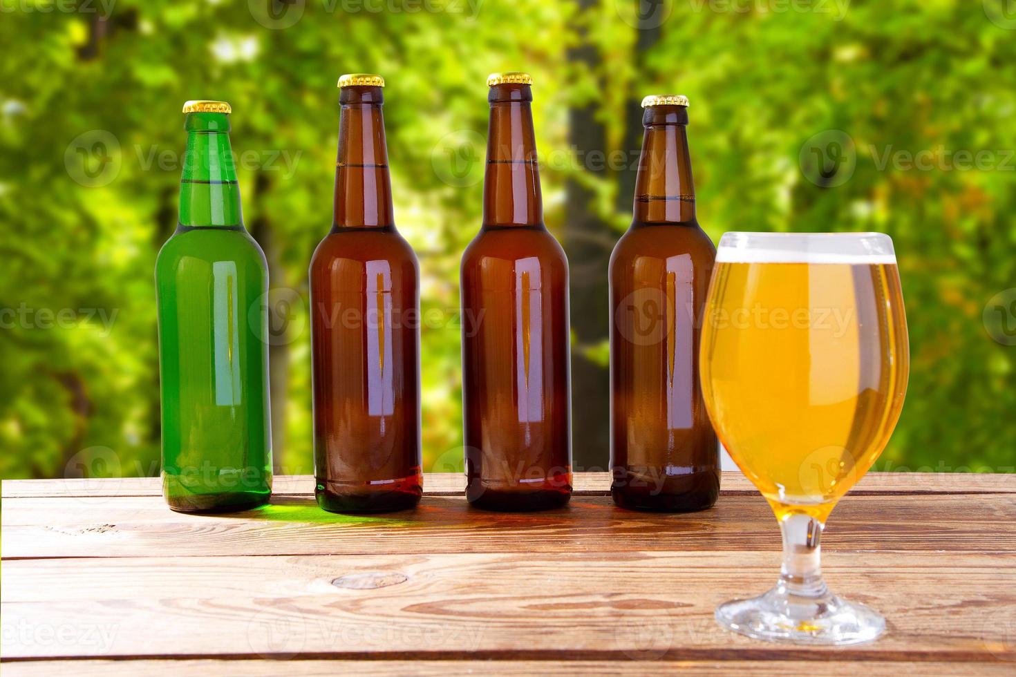 kopp öl och flaskor på trälåda på bordet på suddig parkbakgrund foto