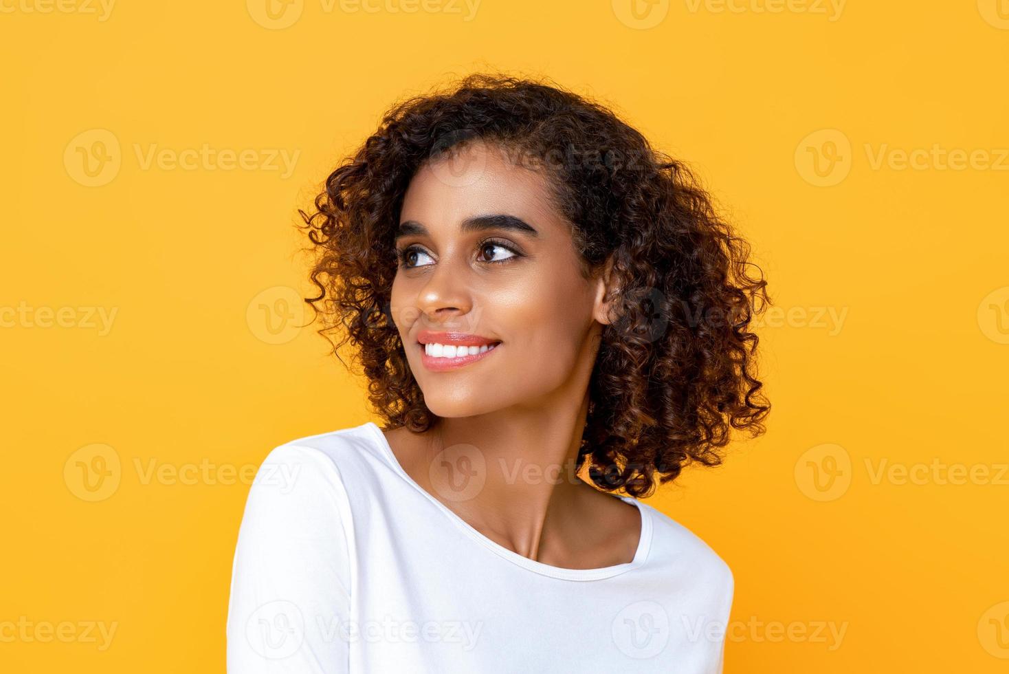 närbild porträtt av leende ung vacker afrikansk amerikansk kvinna som tänker medan hon glatt tittar på sidan i isolerad studio gul bakgrund foto