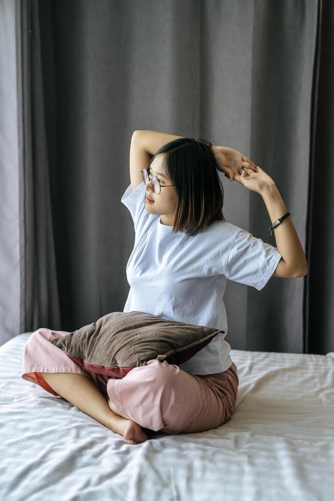 en kvinna i vit skjorta som sitter på sängen och höjer båda armarna. foto