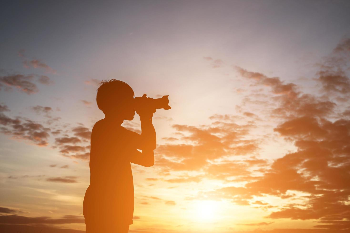siluett av en ung man som håller kameran, sträck ut armarna medan solnedgången. foto