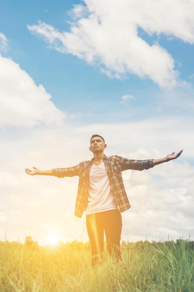 frihet ung tonårsman sträcker sina armar mot himlen njuta och glad med frisk luft på gräsmark. foto