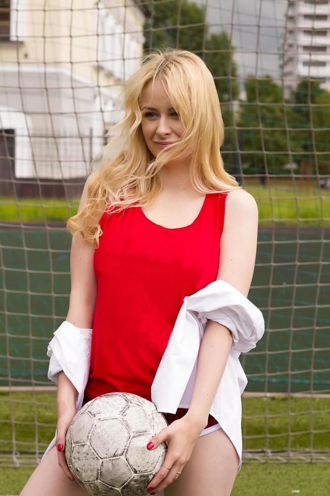 blondinen i röd form med en boll vid grinden på fotbollsplanen. foto