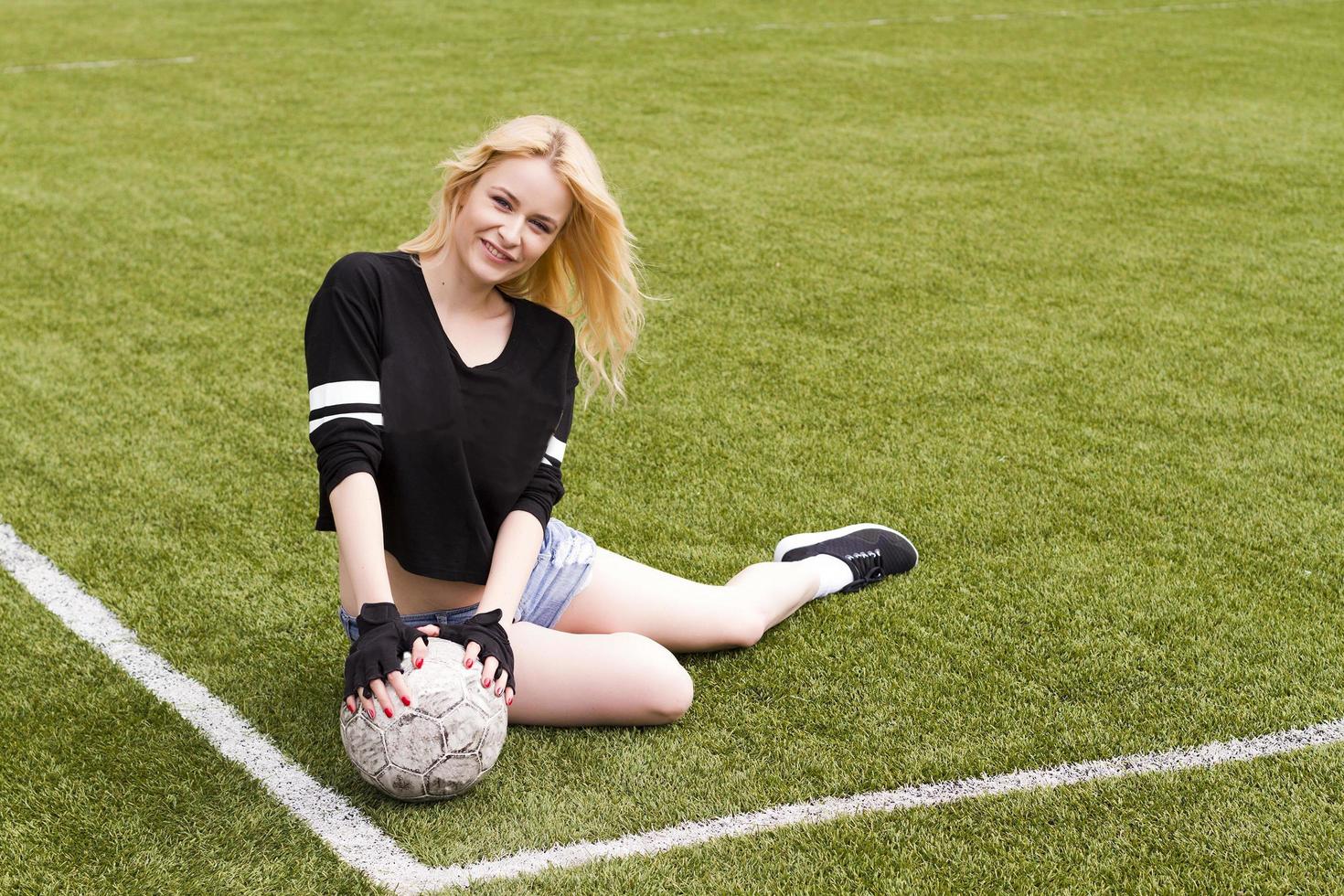 flickan sitter på fotbollsplanen med bollen. foto