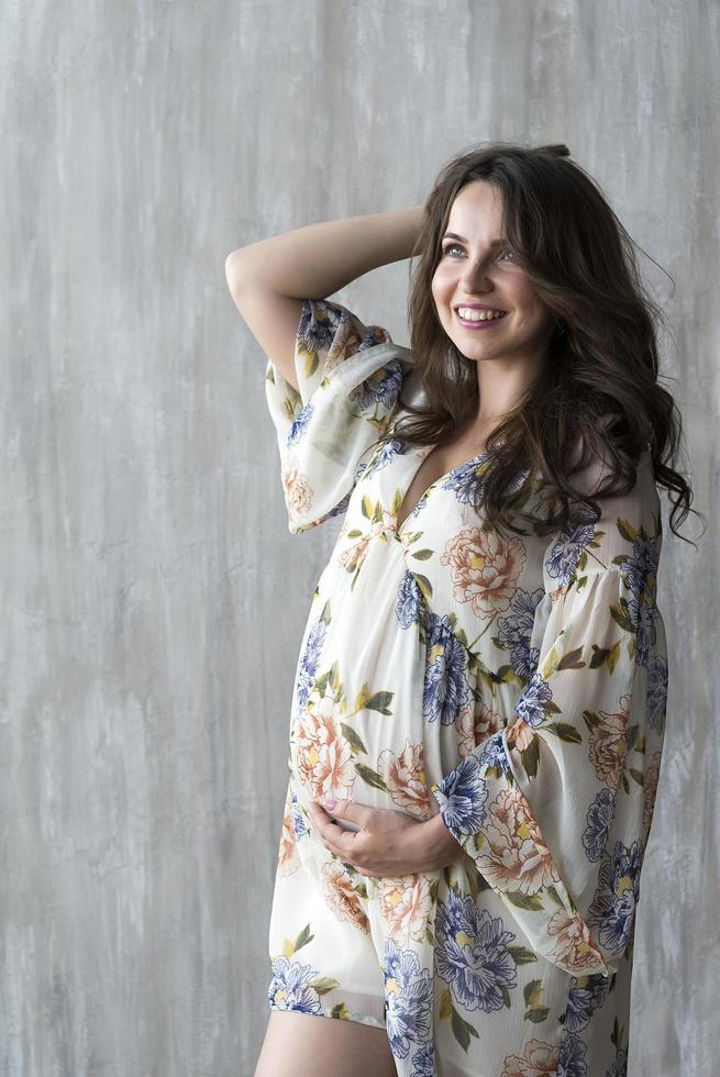 gravid flicka i klänning på grå vägg bakgrund. foto