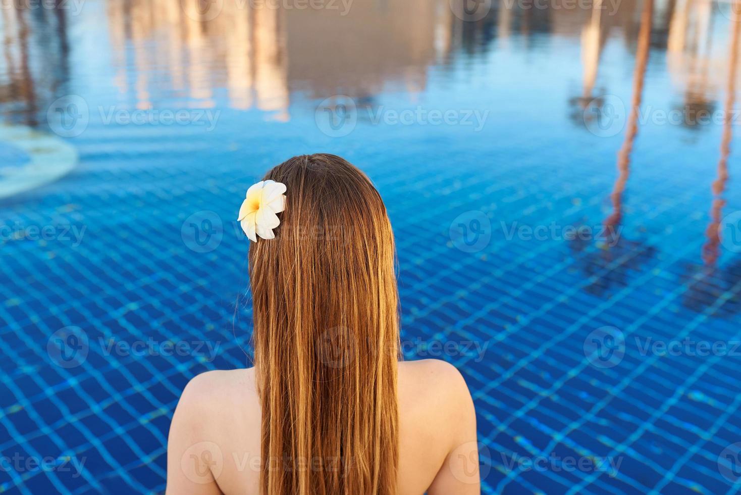 baksidan av kvinnan med blomma sitter på kanten av poolen. foto