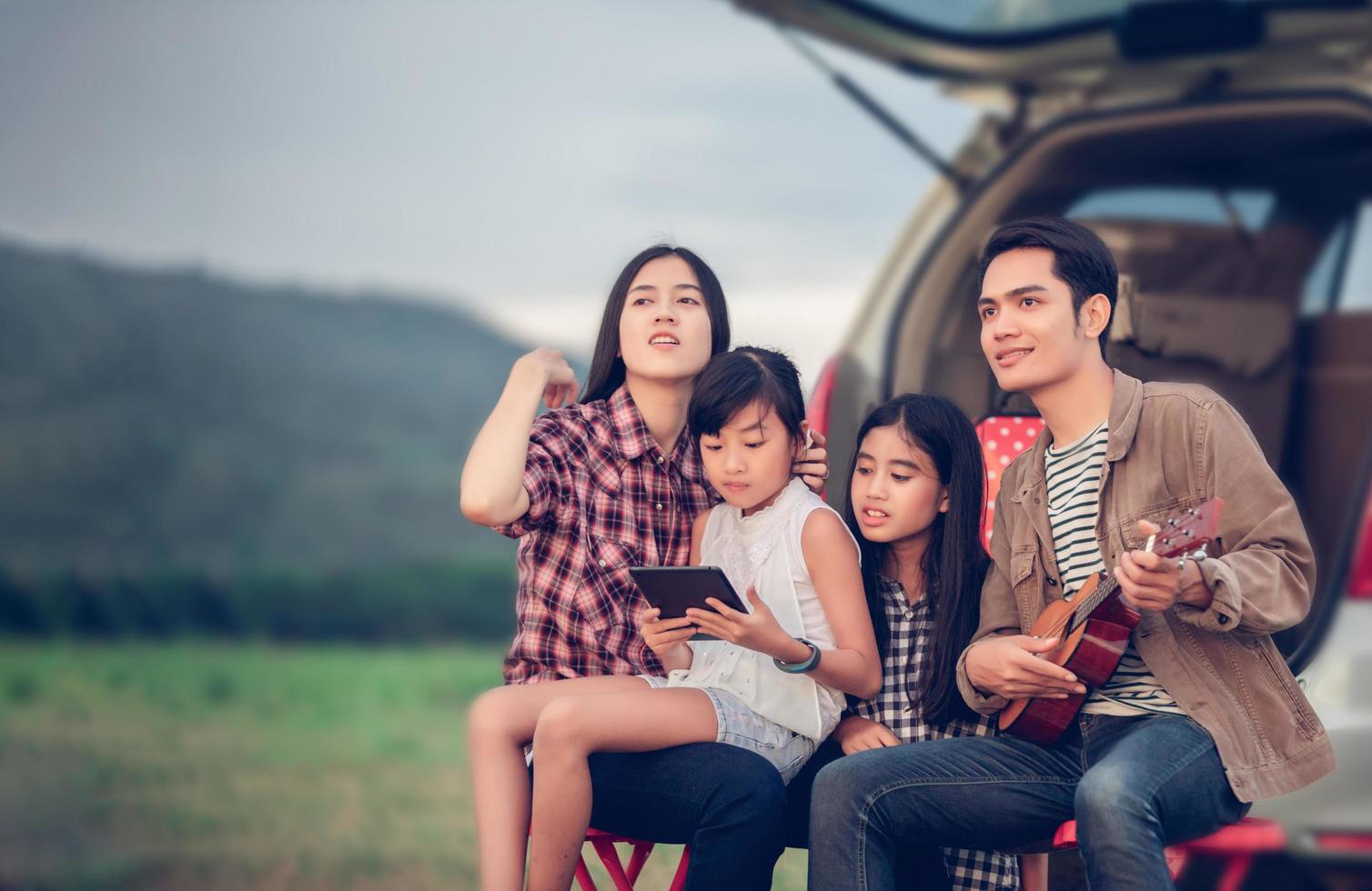 glad liten flicka som leker ukulele med asiatisk familj som sitter i bilen för att njuta av roadtrip och sommarlov foto