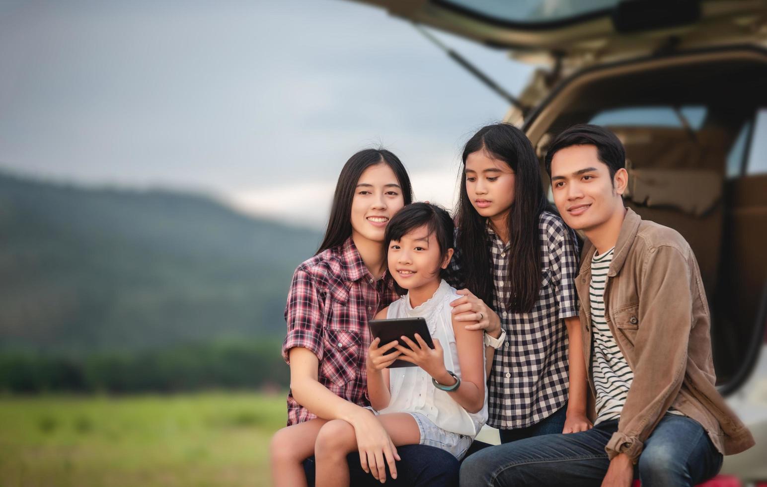 glad liten flicka med asiatisk familj som sitter i bilen för att njuta av roadtrip och sommarlov i husbil foto