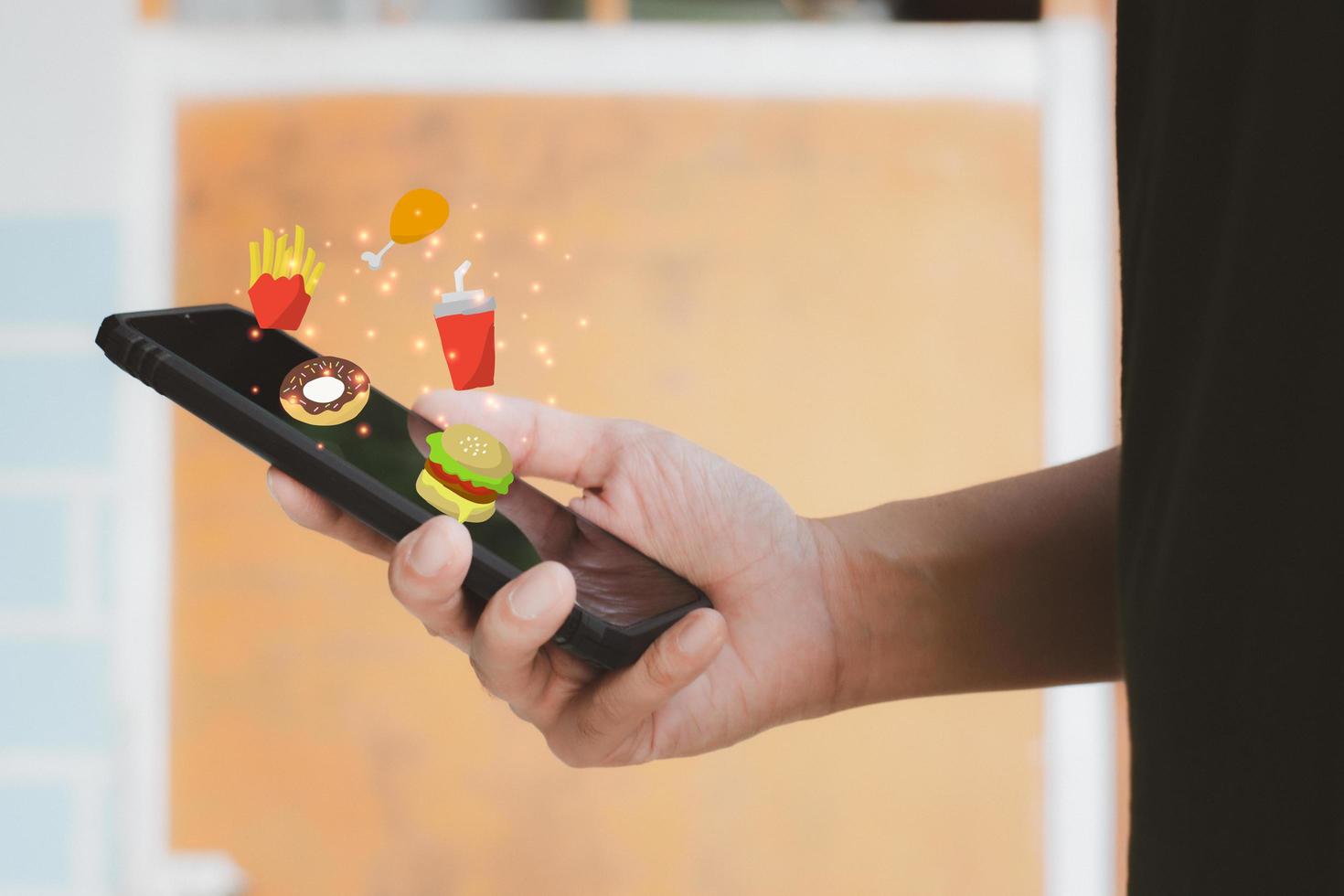 mat leverans koncept. hand som håller svart smartphone eller mobiltelefon och mat tecknad ikon för att söka efter lunch eller middag. nätmat i ny normal. foto