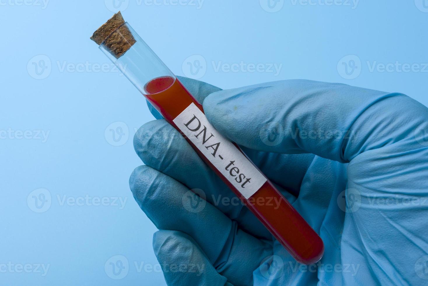 hand som håller ett dna-test i ett provrör på en blå bakgrund. foto