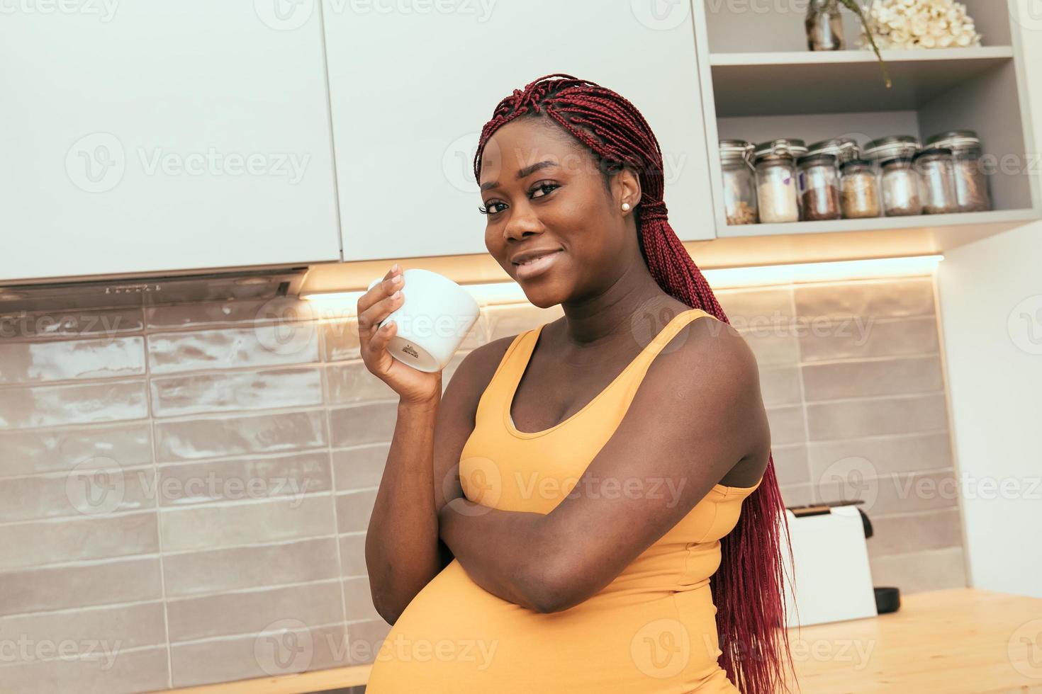 svart gravid kvinna tar en kopp kaffe i köket foto