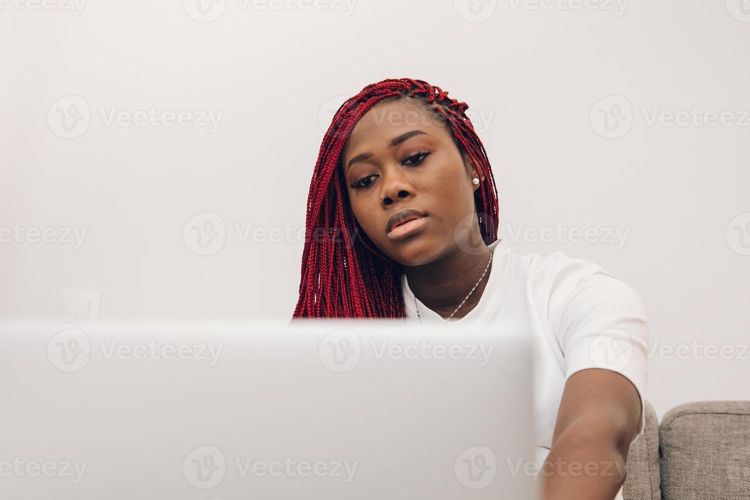 svart gravid kvinna kopplar av på soffan hemma med sin bärbara dator foto